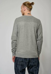 Pull grise à manches longues avec un relief texturé sur les épaules et les manches, associé à un pantalon sombre à motifs. Design simple et décontracté.