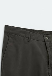 Taille et partie supérieure d'un pantalon gris foncé avec bouton, fermeture éclair, passants de ceinture et poches avant sur un fond clair.