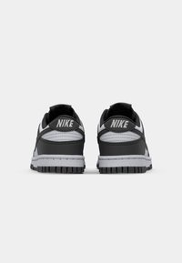 Nike sneakers with a black upper, grey accents, textured materials, and a grooved black rubber sole; features "NIKE" branding on the heel.