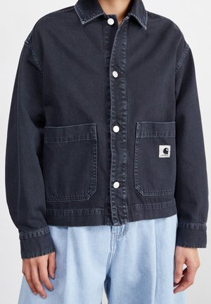 Person wearing a dark denim jacket with silver snap buttons, two front pockets, and light blue jeans, cropped at the waist.