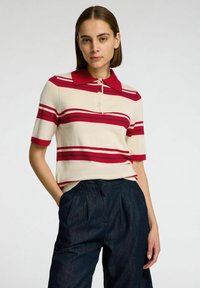 Polo shirt in crèmekleur met rode en marineblauwe strepen, voorzien van een rode kraag en drie knopen. Gepaard met donkerdenim plooibroek.