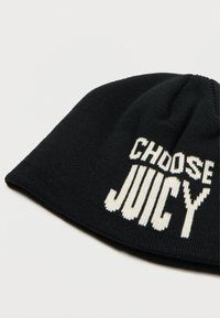 Berretto di lana nera con testo bianco e bold "CHOOSE JUICY" sul davanti, posato su una superficie chiara e semplice.