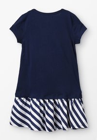 Laivastonsininen lyhythihainen mekko, jossa on raidallinen valkoinen ja laivastonsininen röyhelöhäntä. Sileä puuvillakangas, pyöreä pääntie, rento muotoilu.