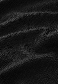 Tissu noir texturé avec de fines nervures verticales irrégulières créant des vagues douces et fluides ainsi que des ombres sur la surface.