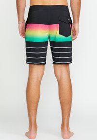 Shorts de bain noirs avec un design dégradé présentant du rose, du vert et du jaune en haut. Rayures blanches horizontales en bas et sur la poche arrière.