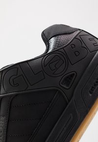 Sneaker nera con tomaia in pelle texturizzata, suola in gomma e vistoso marchio "GLOBE". Presenta un collare imbottito e sottili accenti a motivo.