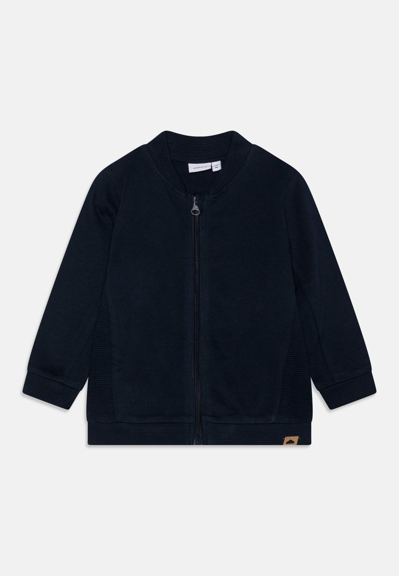 Veste zippée bleu marine foncé avec col et poignets côtelés. Texture lisse, design à panneaux latéraux et petite étiquette logo sur le côté inférieur.
