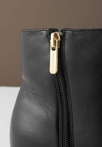 Černé kožené kotníkové boty s detaily zlatého zipu a texturovaným povrchem. Boční zip zdůrazňuje elegantní design.