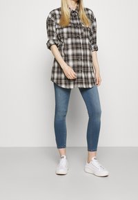 Camisa a cuadros en blanco y negro, con botones y mangas enrolladas, combinada con jeans skinny azules y zapatillas blancas para un look casual.