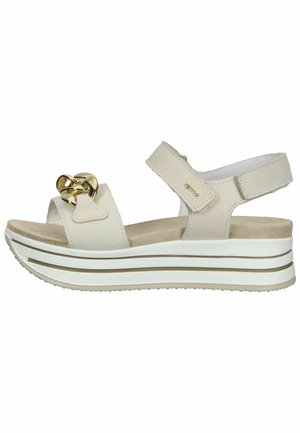 Beige kile sandals med tyk hvid sål, justerbar ankelrem, og forreste rem dekorert med stort skinnende guld kæde.
