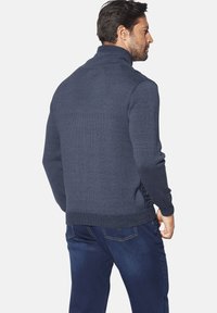 Marineblauer gestrickter Sweater mit hohem Kragen, strukturiertem Stoff und gerippten Bündchen; taillierte Passform mit subtilen seitlichen Details.