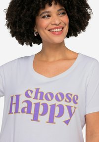 Hvid kortærmet t-shirt med v-hals, der har teksten "choose Happy" i lilla og gule omridsbogstaver. Blød tekstur.