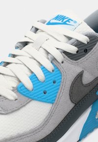 Nike sneaker featuring a gray and white mesh upper with blue accents, textured blue and gray panels, and white laces.