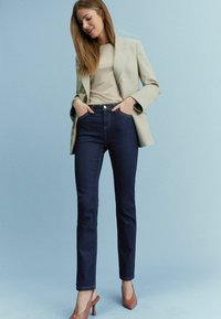 Tmavomodré džínsy so Slim fit strihom, skombinované s béžovým topom a svetlozeleným blejzrom. Džínsy majú predné vrecká a zapínanie na gombík.