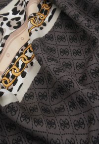 Zijden sjaal met een mix van zwart, beige en gouden patronen; heeft dierenprint, kettingen en intricate geometrische ontwerpen op een gestructureerd oppervlak.