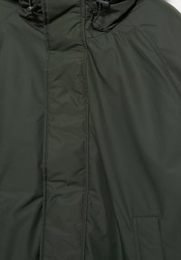 Jachetă căptușită verde închis, cu fermoar frontal acoperit de un flap de furtună și glugă ajustabilă cu șnururi de reglare.