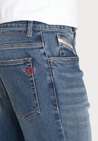 Mörkblå denimjeans för män med en lätt blekning, orange sömmar, en röd logotag på bakfickan och en klassisk femficksdesign.