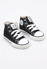 Zwarte canvas sneakers met hoge schacht, witte rubberen teentips, contrasterende stiksels en witte veters. Heeft een cirkelvormig logo aan de zijkant.