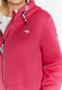 Felpa con zip fucsia con finitura testurizzata, cappuccio con coulisse e logo ombrello ricamato sul petto. Tessuto morbido, design casual.