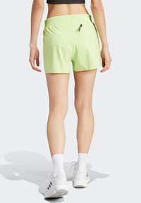 Jasnozielone sportowe spodenki z elastycznym pasem i małą kieszonką na zamek z tyłu, noszone z białymi butami i skarpetami.