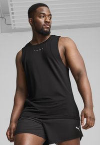 Camiseta de tirantes negra atlética con cuello redondo y logotipo blanco centrado en el pecho, combinada con pantalones cortos negros con acentos de logotipo blanco.