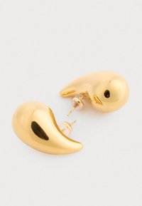 Náušnice v zlatej farbe v tvare abstraktných vtákov, s lesklým povrchom, malými čiernymi akcentmi ako oči a s pätkami na pripevnenie.
