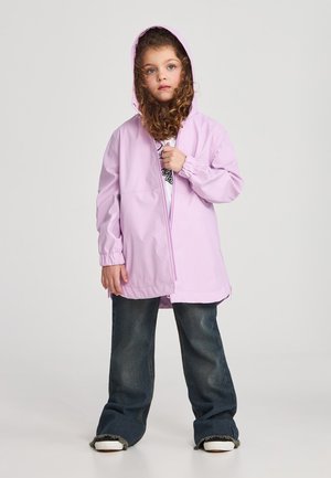 Giacca a vento rosa chiaro con cappuccio, zip completa, polsini elasticizzati e vestibilità morbida, abbinata a jeans a gamba larga blu scuro e sneaker bianche.