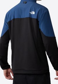 Fleece jacket with a blue upper and black lower section. Features a high collar, long sleeves, and a logo on the back. Textured fabric.