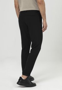 Zwarte taps toelopende broek van een gestructureerde stof, met een subtiel patroon, zijzakken en opgerolde manchetten, gecombineerd met zwarte sneakers.