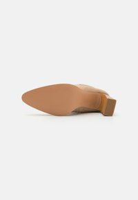 Bottines en daim beige avec un bout carré et un petit talon épais. La semelle est marron clair avec une texture lisse et un léger motif de grip.
