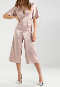 Hedvábný růžový overal s širokými krátkými rukávy, hlubokým výstřihem do V a zkrácenými širokými nohavicemi. V páru s metalickými vysokými podpatky.