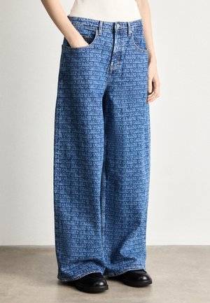 Világoskék denim széles szárú farmernadrág, amely texturált, ismétlődő logó mintázattal rendelkezik. Elöl zsebekkel és gombos záródással felszerelve.