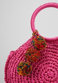Sac à main rond rose tissé avec trois pompons multicolores attachés près de la poignée.