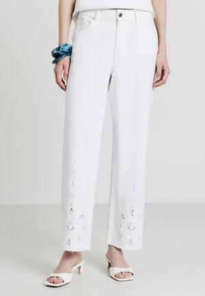 White denim pants with a straight-leg cut, featuring floral embroidery at the cuffs and frayed edges. Paired with white open-toe heels.