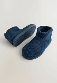 Et par marineblå fleece ankel-sandaler med gummisåler, hvor den ene sandal står oprejst, mens den anden ligger på siden.