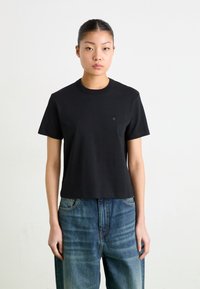 Camiseta de algodón negra con cuello redondo y mangas cortas. Presenta un pequeño logo en el pecho. Combinada con unos vaqueros de denim azul de corte holgado.