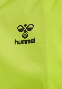 Limegrön tyg med en svart Hummel-logotyp och en abstrakt bi-design ovanför varumärket, som visar en jämn textur och en livlig färg.
