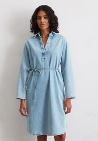 Robe en denim bleu clair avec un col, des manches longues et une taille cintrée. Elle présente une patte de boutonnage avant et des coutures contrastantes au niveau de l'ourlet.