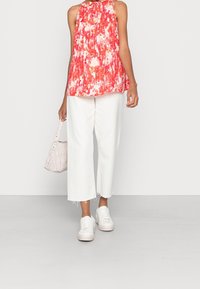 Haut fluide à fleurs rouges et roses avec col licou, associé à un pantalon blanc court, des baskets blanches et un sac à main rose clair texturé.