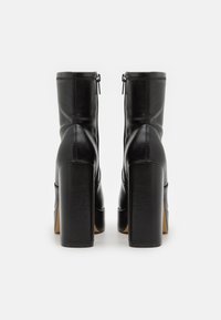 Black leather ankle boots with a zip closure, square heels, structured design, and subtle stitching detail. Smooth texture and sleek shape.