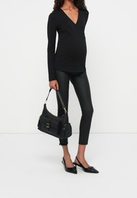 Top negro de manga larga cruzada, pantalones de cuero negros ajustados y bolso negro con herrajes dorados y bolsillos en el frontal. Tacones negros de punta.