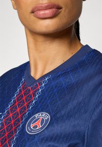 Paris Saint-Germain jersey featuring a deep blue fabric with red and light blue geometric patterns, V-neck design, and a round logo on the chest.