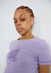 Lilac fitted t-shirt with short sleeves, ribbed texture, and a circular graphic design featuring stylized text and wave accents.