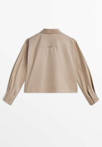 Chemise beige courte à manches longues, avec un col et des poignets boutonnés. Dispose d'une couture d'empiècement au dos et d'une texture de tissu lisse et légère.