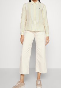 Yellow and white striped button-up shirt with long sleeves, paired with cream wide-leg pants and light beige sneakers.