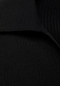Tissu en tricot noir avec une texture côtelée et un détail de col replié. Le matériau semble doux et légèrement extensible.