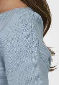 Light blue knitted sweater with ribbed neckline, textured shoulder seams, and smooth body. Soft, lightweight fabric, emphasizing modern design.
