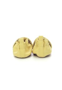 Chaussures pour bébés en cuir jaune avec une forme arrondie, un design froncé à l'avant et de courtes languettes à l'arrière. Texture lisse ; matériel minimal.