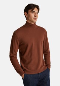 Brązowy sweter z golfem z miękkiego materiału, dopasowany krój, prążkowany kołnierz i mankiety, w zestawieniu z ciemnymi dżinsami dla casualowego wyglądu.