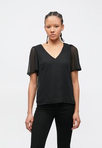 Μαύρη μπλούζα με V λαιμόκοψη, κοντά διάφανα μανίκια και άνετη γραμμή. Το ύφασμα έχει ομαλή υφή και είναι ελαφρύ, κατάλληλο για στιλιστικές στρώσεις.